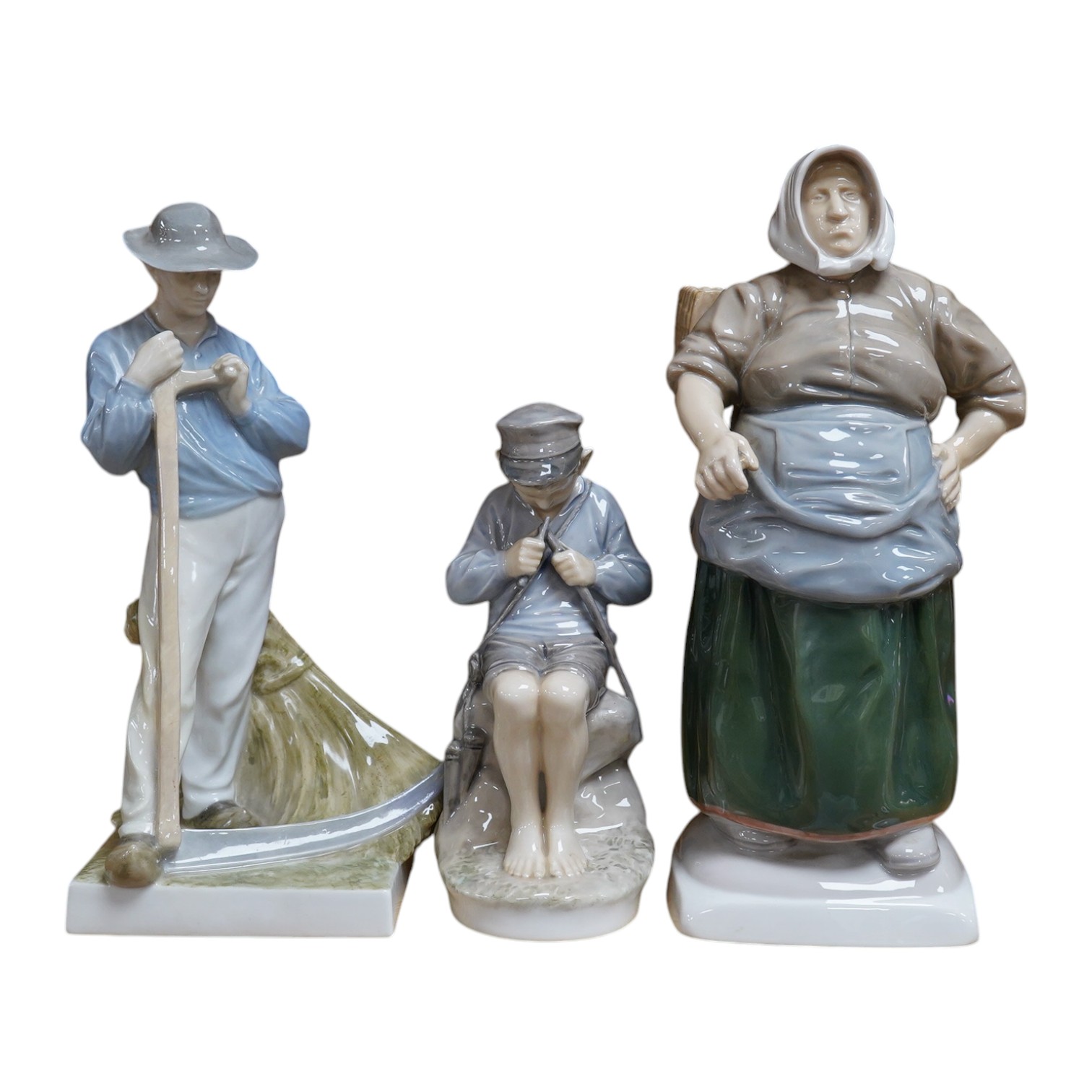 Two Royal Copenhagen figures of a farmer holding a scythe, model number 685, a boy whittling a stick, model 905, together with a Bing and Grondahl figure of a woman, model number 1702, tallest 28cm (3). Condition - good